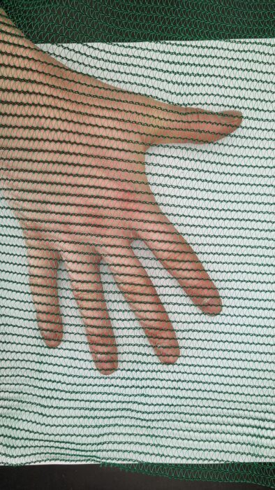 A hand is shown through the mesh of a screen.