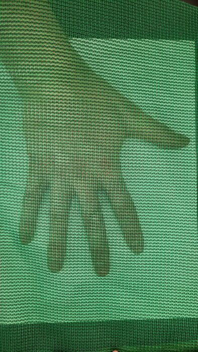 A hand is shown through the mesh of a screen.