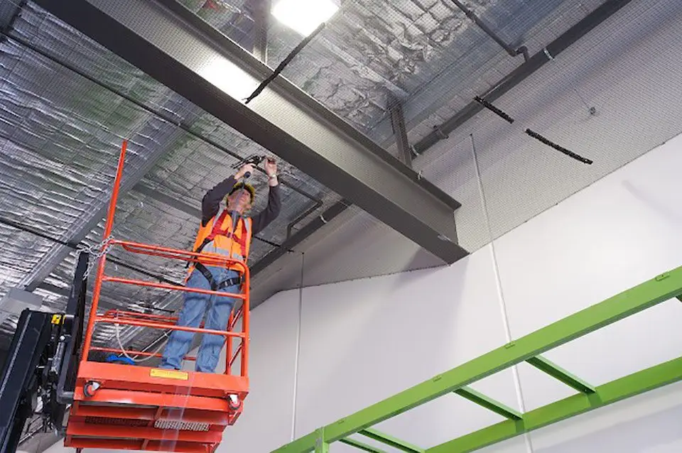 Man on scissor lift installing bird netting in roof of warehouse